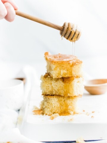 the pieces of corn bread stacked on top of each other with honey drizzling over it.