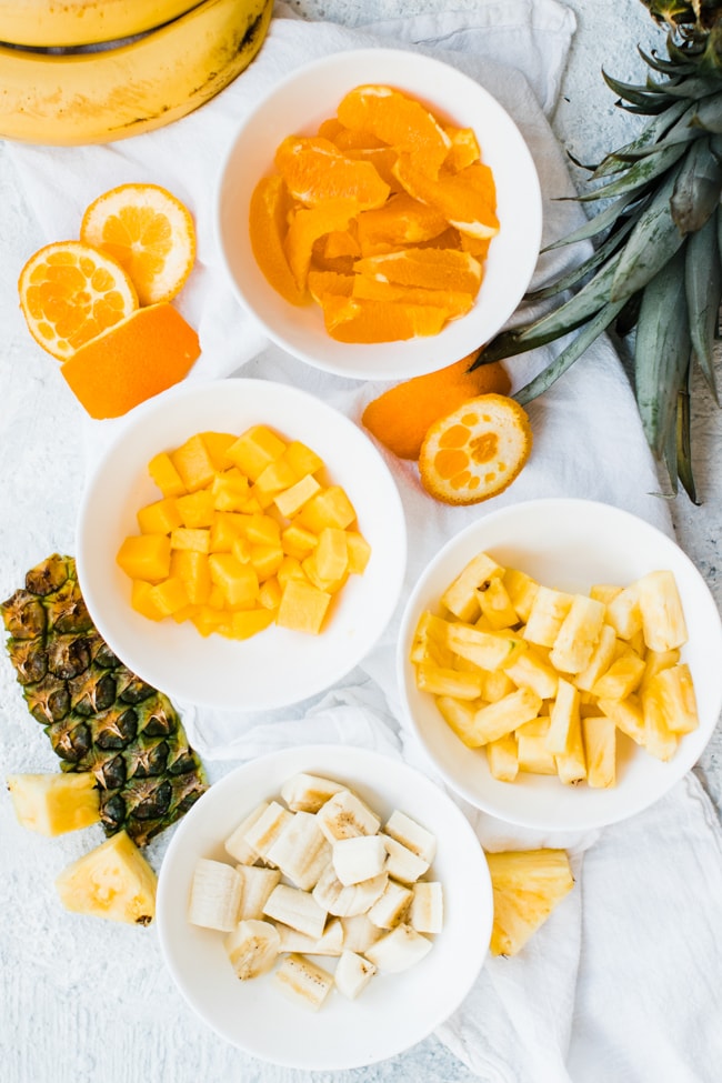 oranges, mango, pineapple, bananas in separate bowls