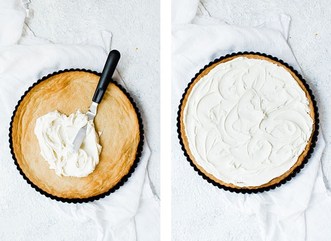 spatula spreading white frosting on sugar cookie crust