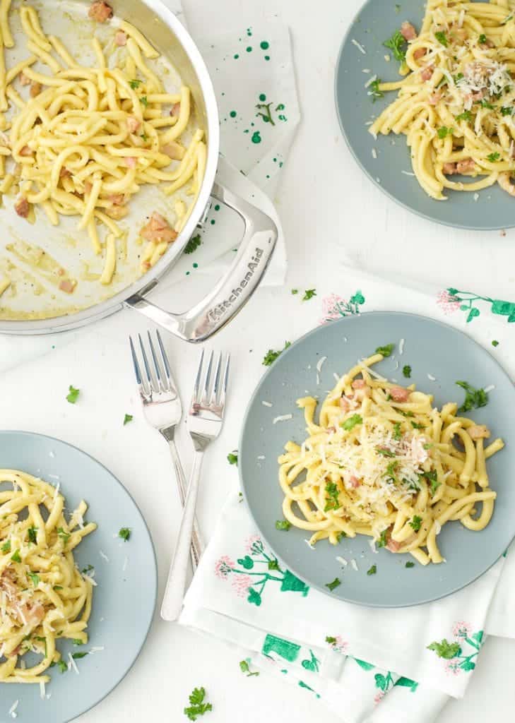 An overhead shot of bucatini carbonara on 3 blue plate and in a large pan