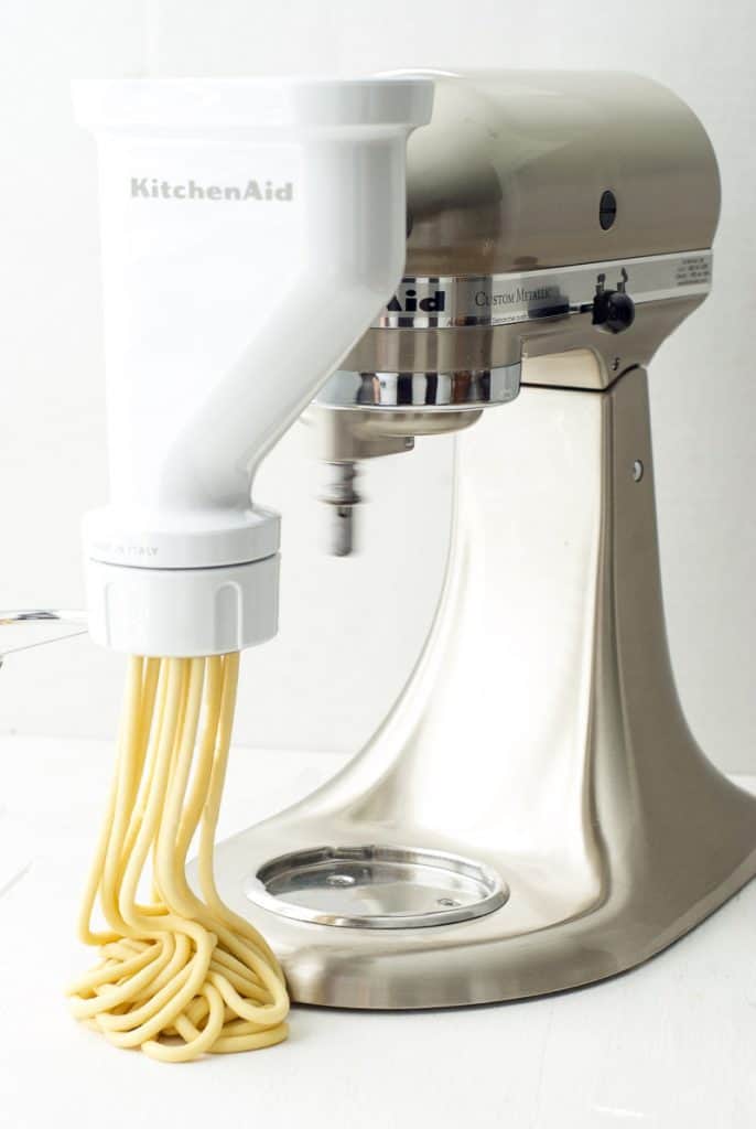 A photo of a kitchenaid with a pasta press making homemade bucatini carbonara