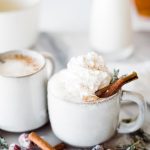 one cup in focus with cinnamon sticks and whipped cream topping