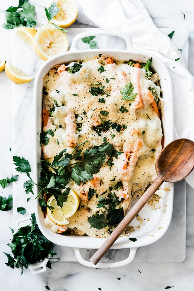 Quinoa bake in a white casserole dish. The dish is garnished with parsley and lemons.