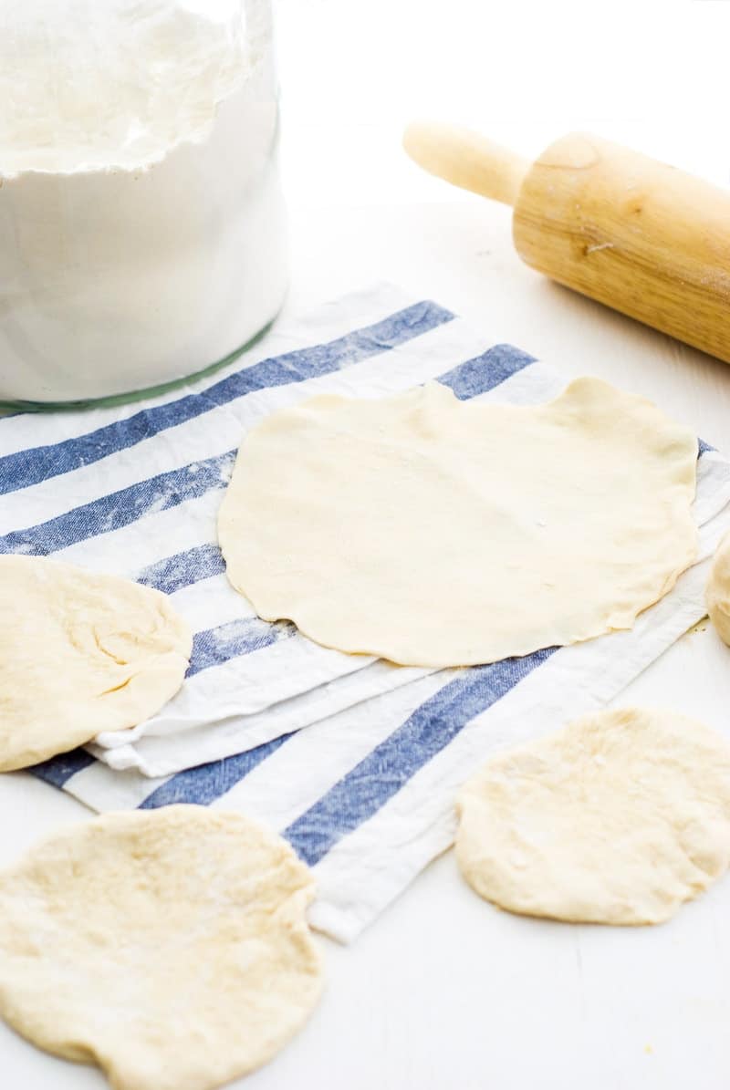 A photo of homemade flour tortillas getting rolled out with a rolling pin