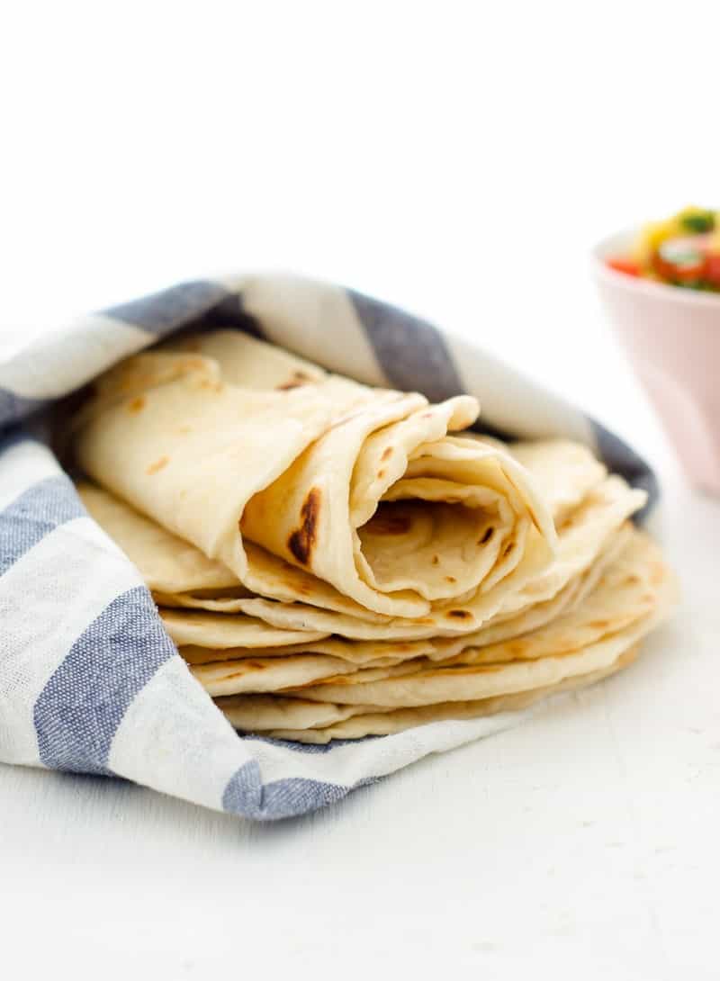 A photo of homemade flour tortillas rolled into a wrap sitting on a white surface
