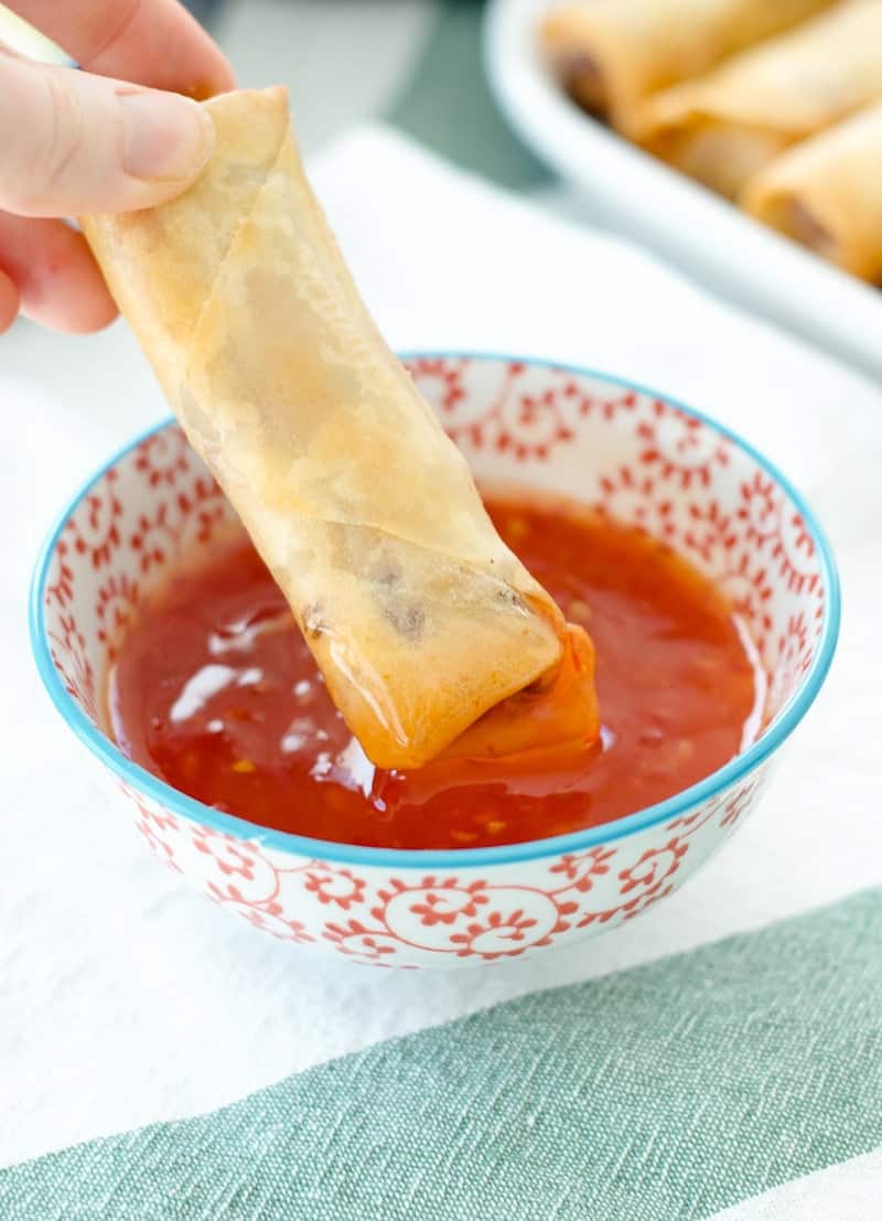 Pork Spring Rolls being dipped into sweet chili sauce 