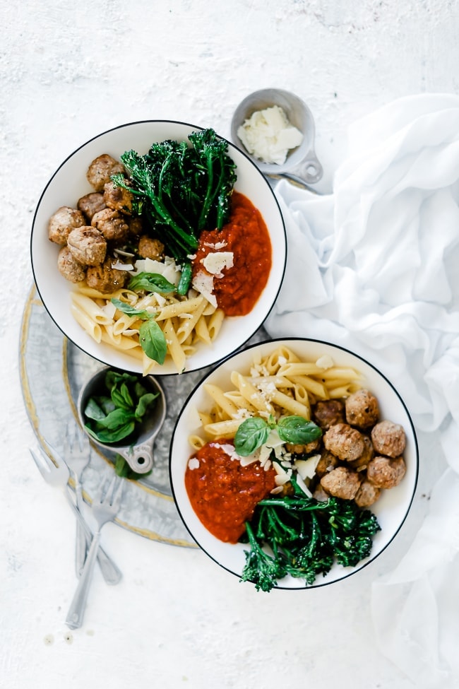 Italian bowl with meatballs and broccoli in rimmed bowls on an aluminum plate.