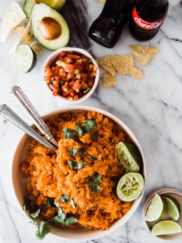 large bowl of orange Mexican rice with limes and cilantro as garnish. two utensils in the bowl
