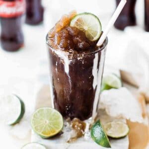A cup of frozen coke with cream dripping down and topped with lime and straw.