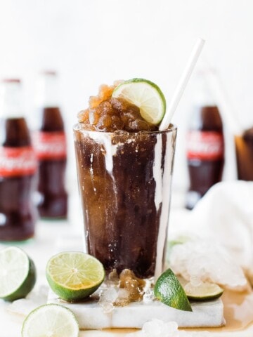 A cup of frozen coke with cream dripping down and topped with lime and straw.