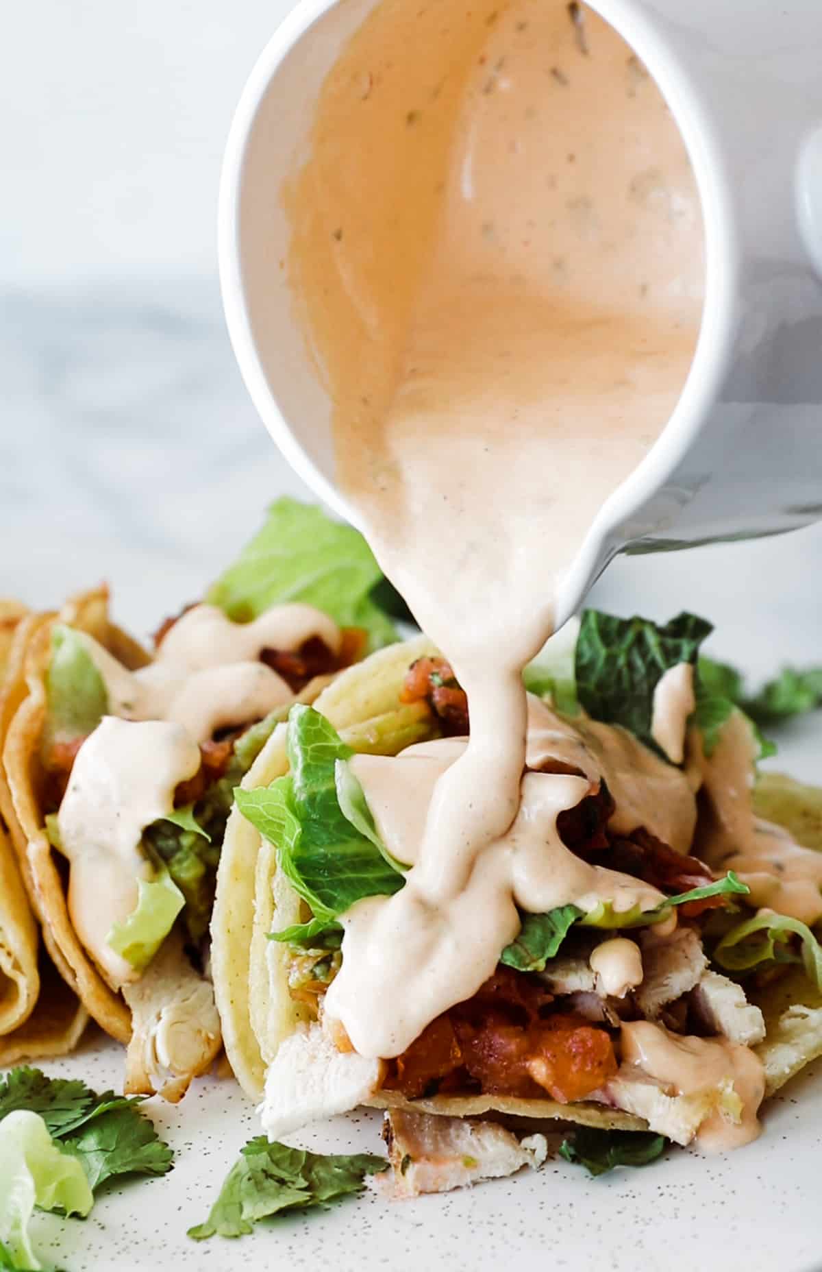 Jar pouring creamy chipotle sauce over a chicken taco