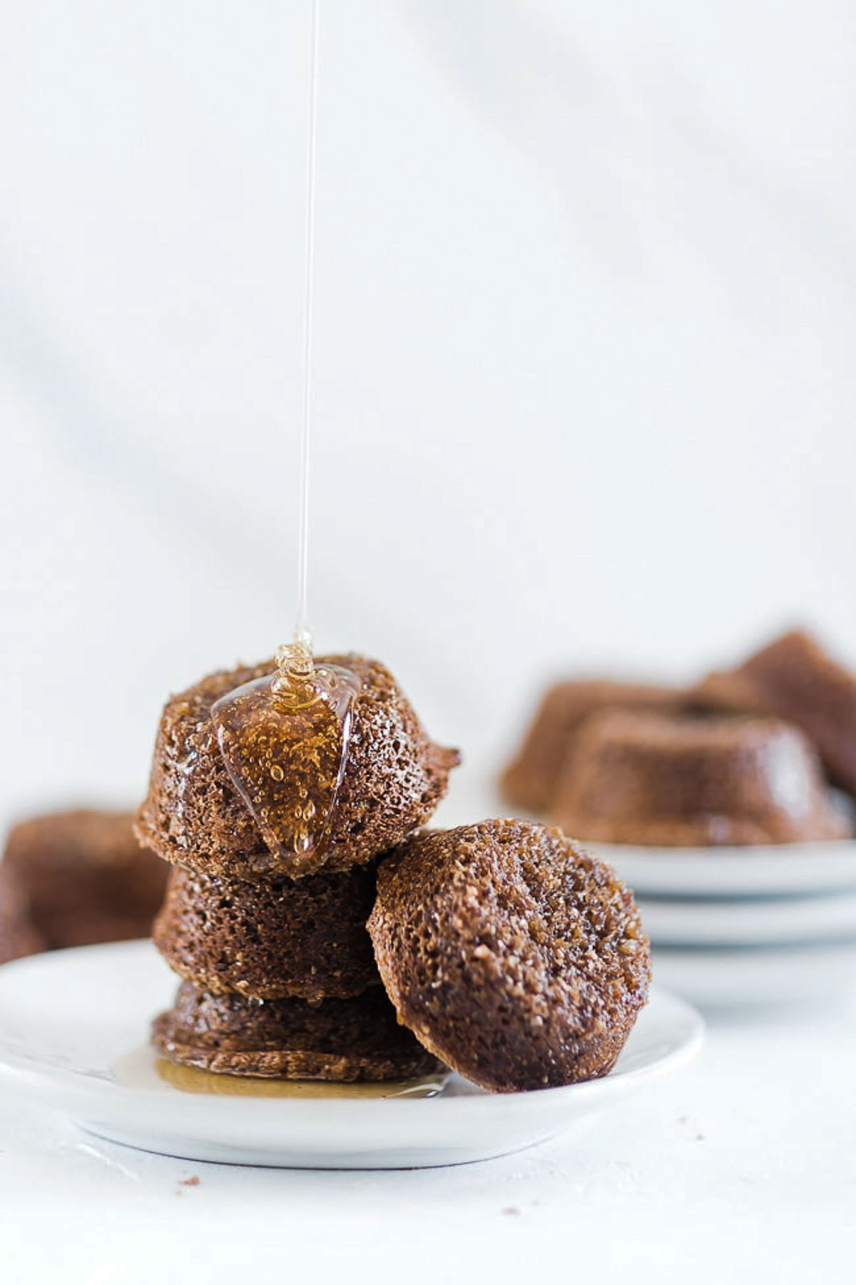 Molasses bran muffins stacked on a white plate. with syrup pouring over top.