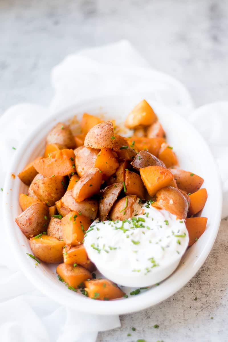 A side shot of seasoned red potatoes on a white serving dish with a white creamy dip at the side