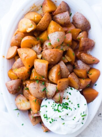 An overhead shot of seasoned red potatoes with a creamy dip at the side
