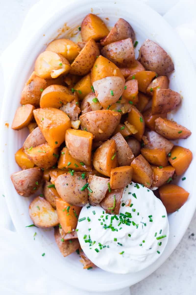 A close up of seasoned red potatoes with a creamy dip and chives on top