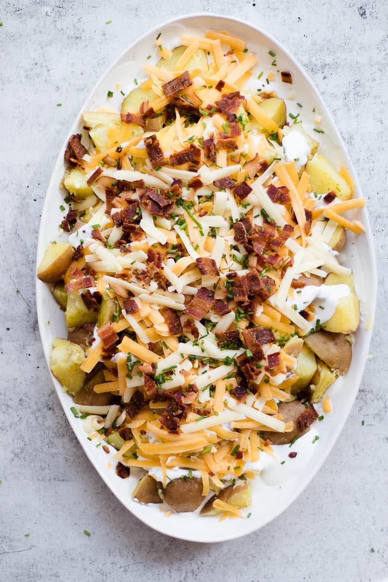 An overhead shot of a cheesy potatoes recipe in an oval baking dish covered with bacon and cheese