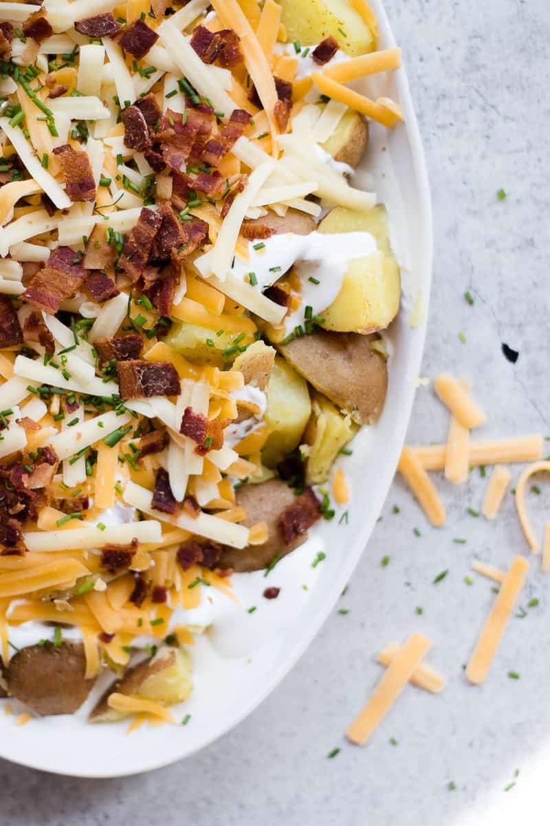 A close up of a cheesy potatoes recipe on an oval baking dish topped with bacon