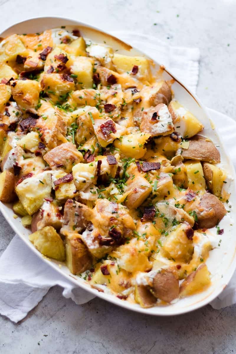 A side shot of a cheesy potatoes recipe topped with bacon, green herbs and cheese