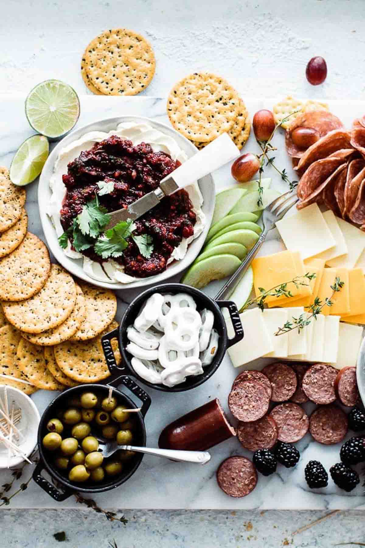 Cranberry salsa with cream cheese in a bowl surrounded by fruit, cheese and crackers.