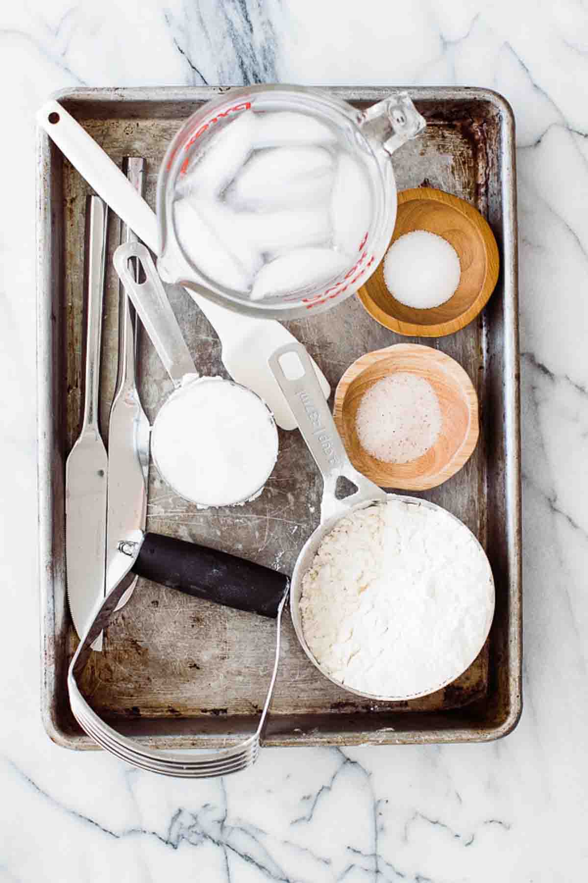 Ingredients to make the best flaky pie crust on a baking tray on the table.
