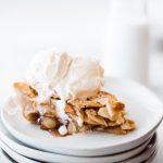 slice of apple pie with ice cream on top on a stack of plates