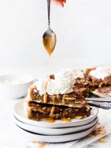 two sliced of pecan pie stacked with whip cream and spoon drizzling over
