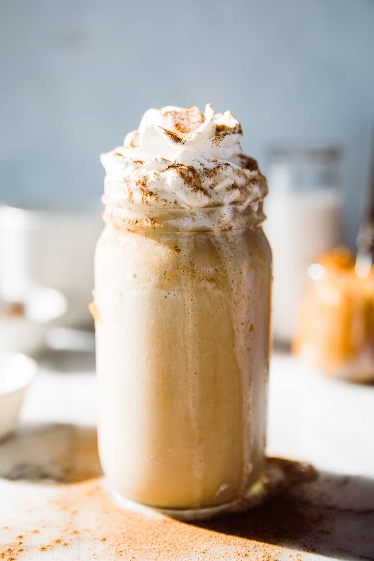 Large glass jar of orange pumpkin smoothie with whip cream and cinnamon topping.
