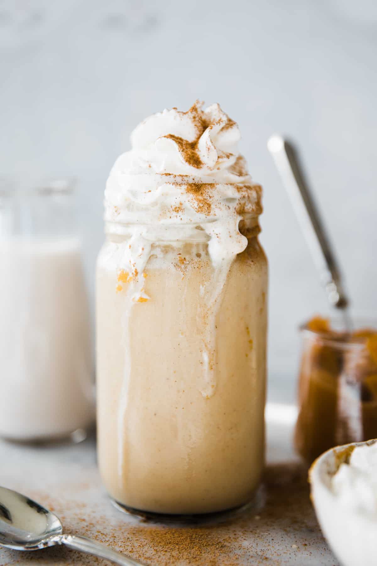 Large glass jar of orange pumpkin smoothie with whip cream and cinnamon topping.