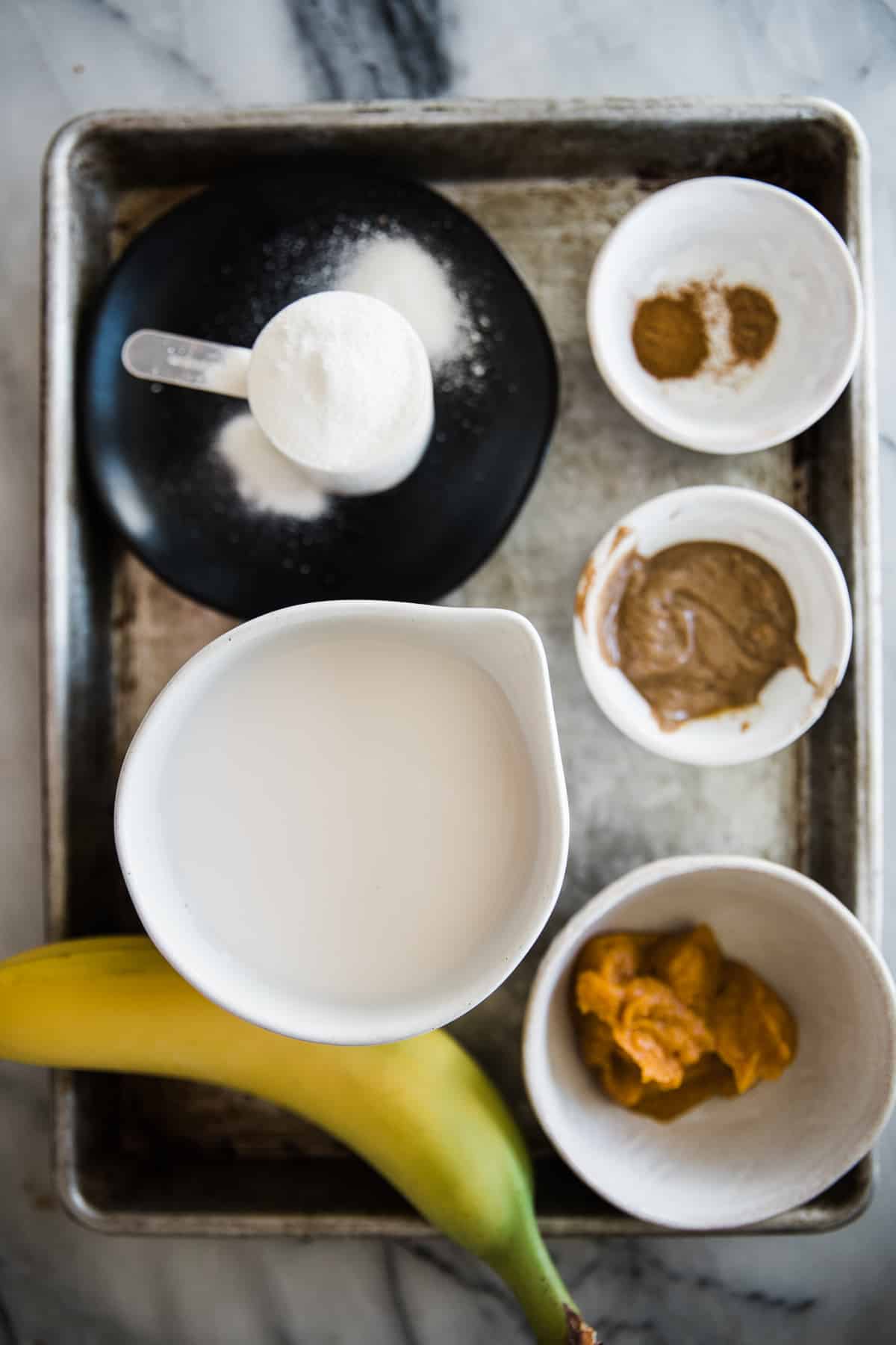 Ingredients on a tray for pumpkin protein smoothie. Included parties powder, milk, pumpkin puree, banana. 