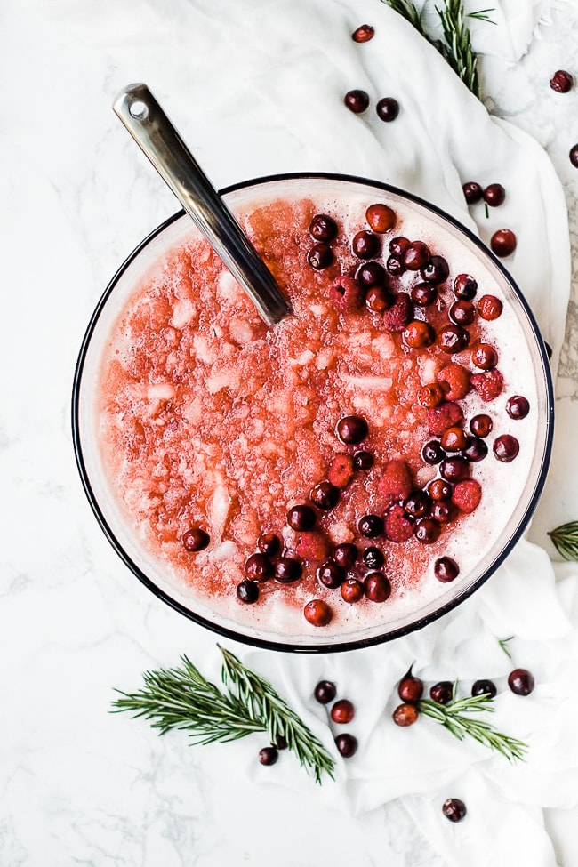 cranberry pineapple slush punch in a punch bowl, garnished with cranberries and raspberries.