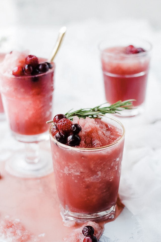 Cranberry pineapple slush punch in glasses. Garnished with rosemary.