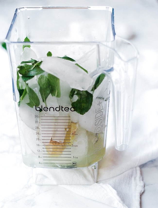 A blender jar filled with ice, limeade, mint, and ginger.