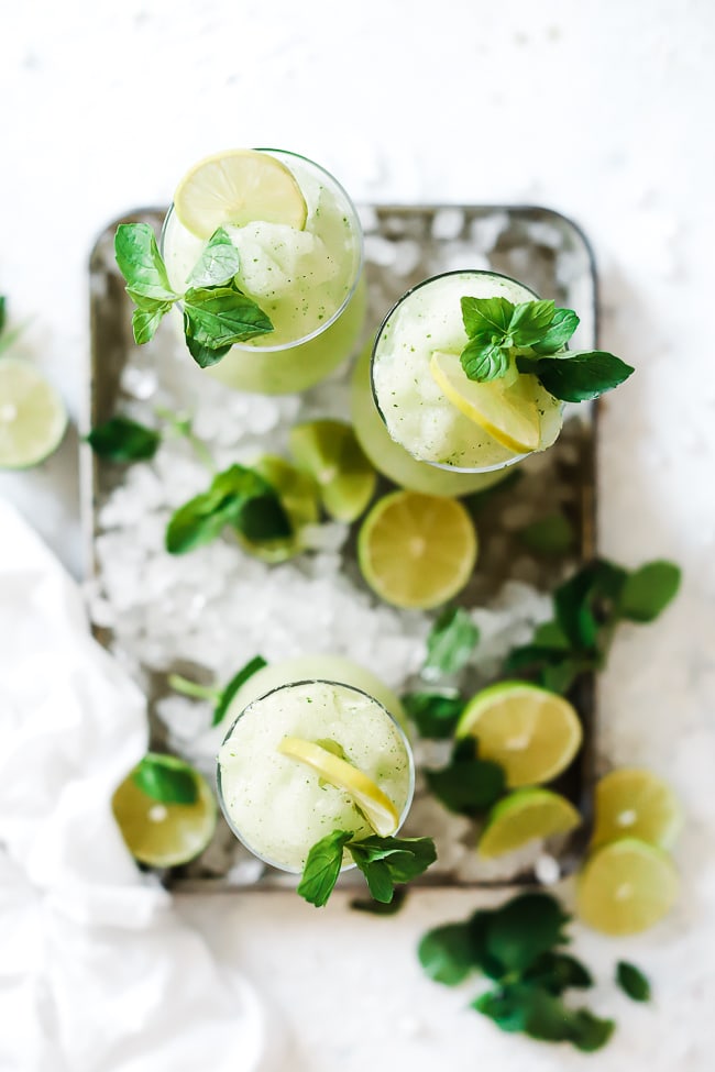 A flat lay of limeade slush in hurricane glasses inside of a baking sheet filled with ice.