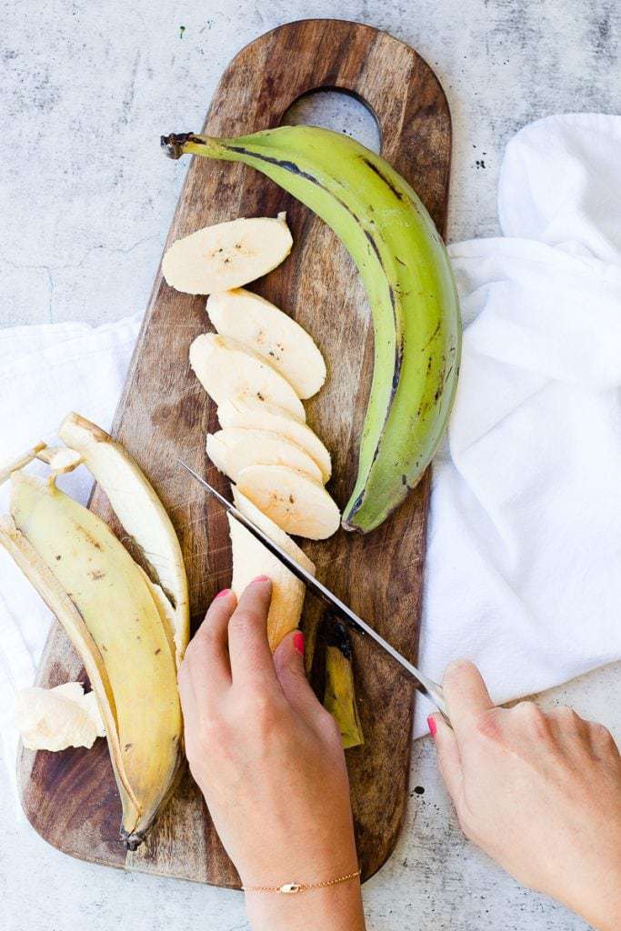 Someone chopping plantains on a wooden board