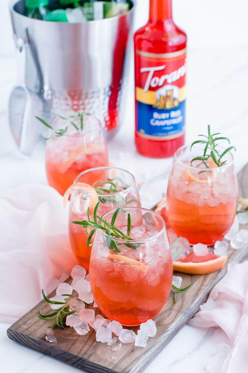 Ruby Red Grapefruit Sparkler cocktails on a wooden board with fruit and ice scattered around