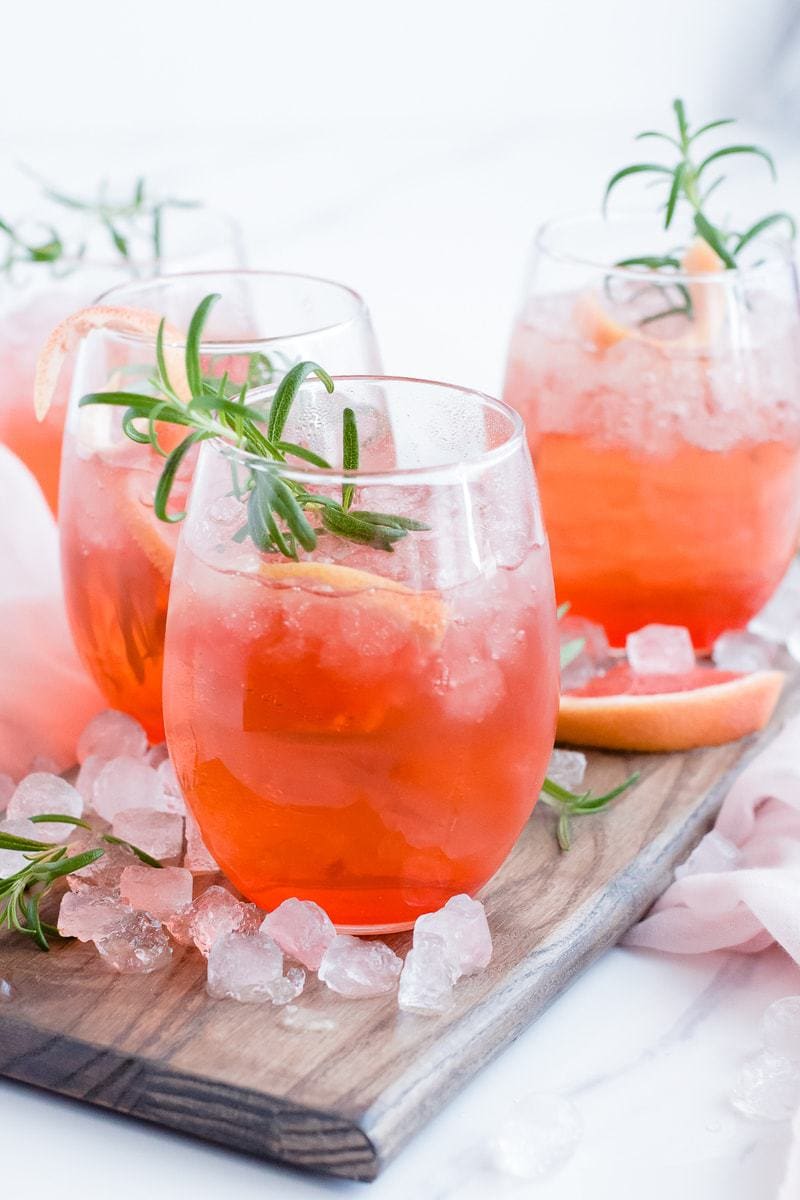 A close up of Ruby Red Grapefruit Sparkler cocktails with ice, grapefruit and rosemary