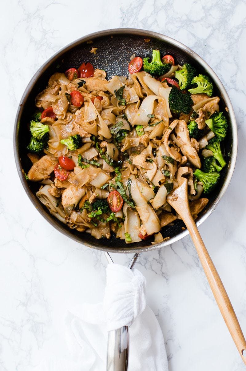 thai drunken noodles in a pan with a wooden spatula 