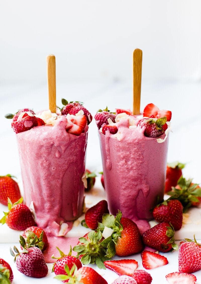 coconut strawberry smoothie in two glasses overflowing onto a white surface
