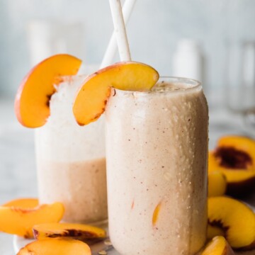 two cups of peach smoothie with peaches slices on garnishes