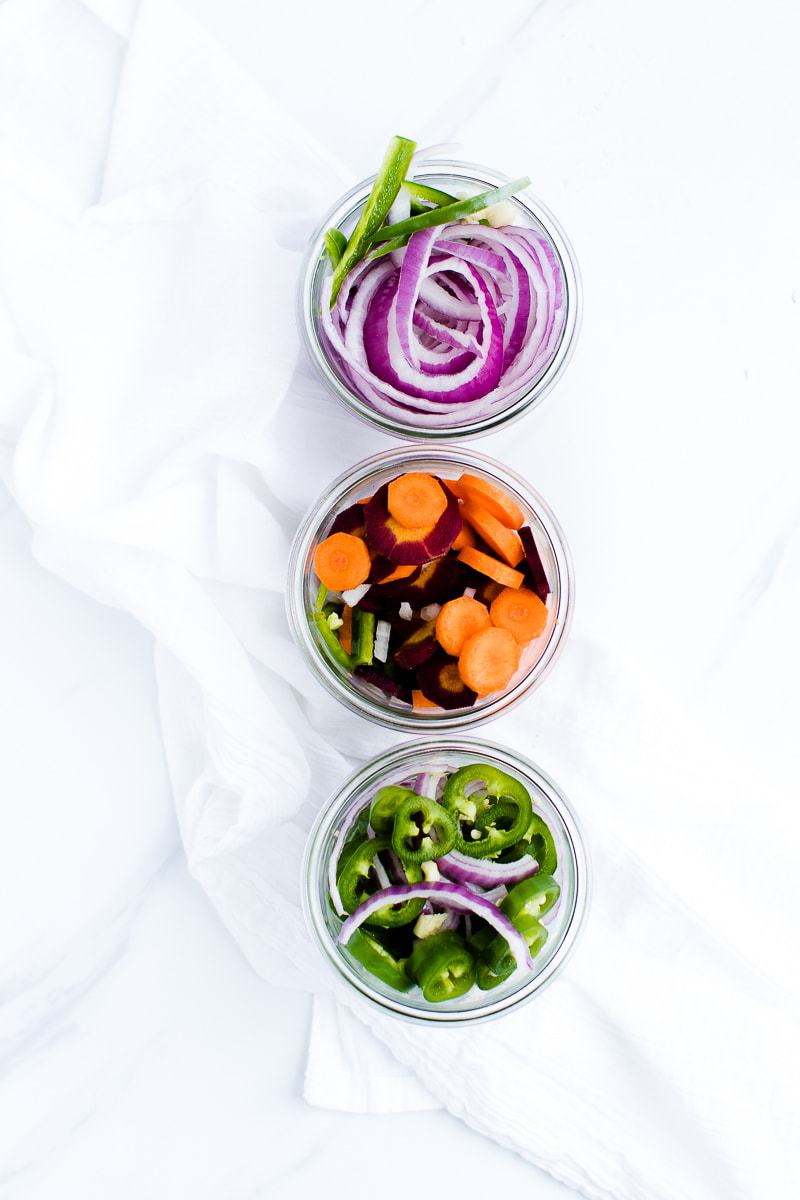 An overhead shot of three jars of pickled red onions and pickled vegetables