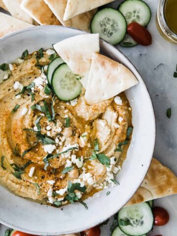 one large bowl of creamy hummus with feta and basil topping. Pita bread on the side.