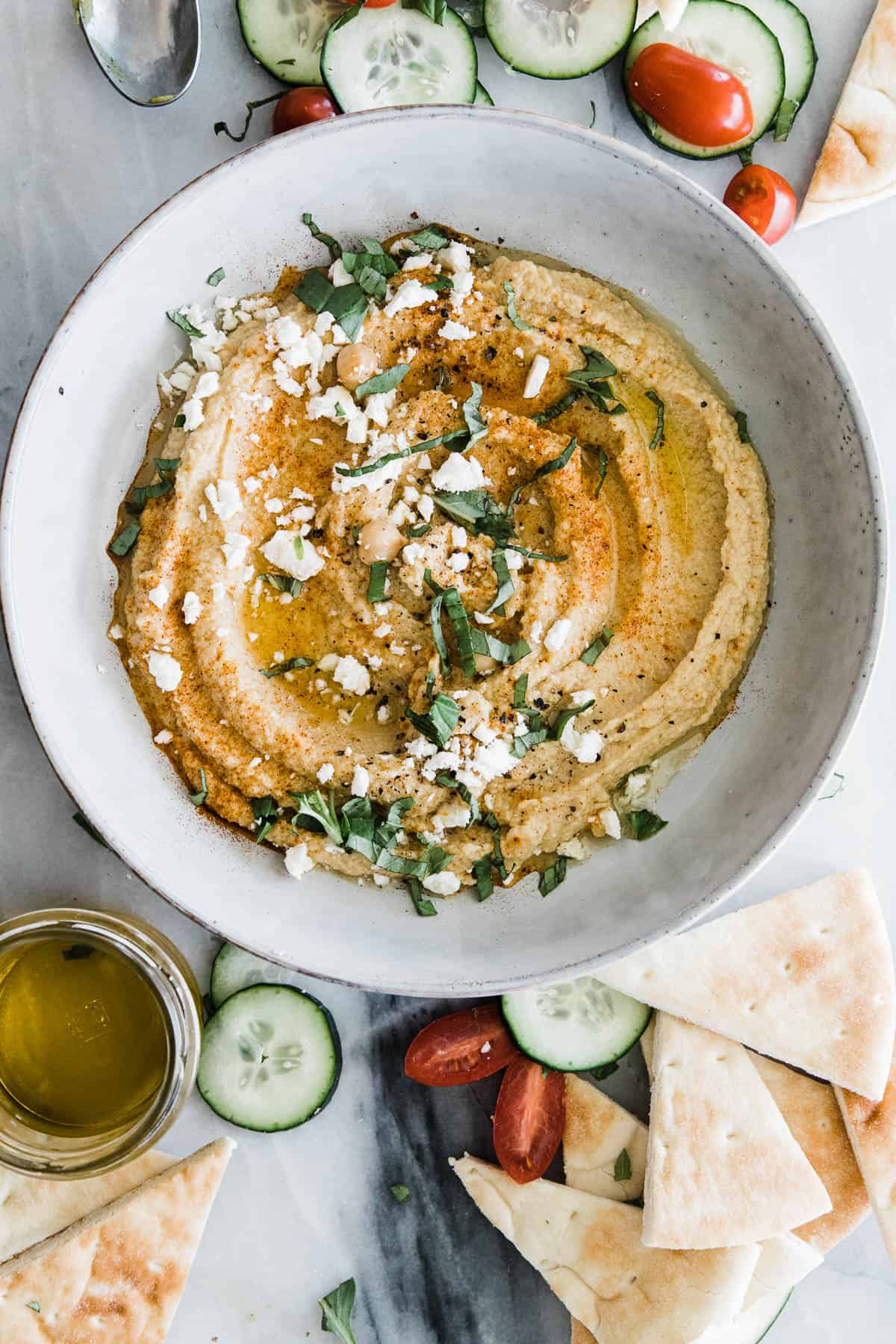 A bowl of easy hummus on the table topped with olive oil, black pepper, cheese, and herbs.