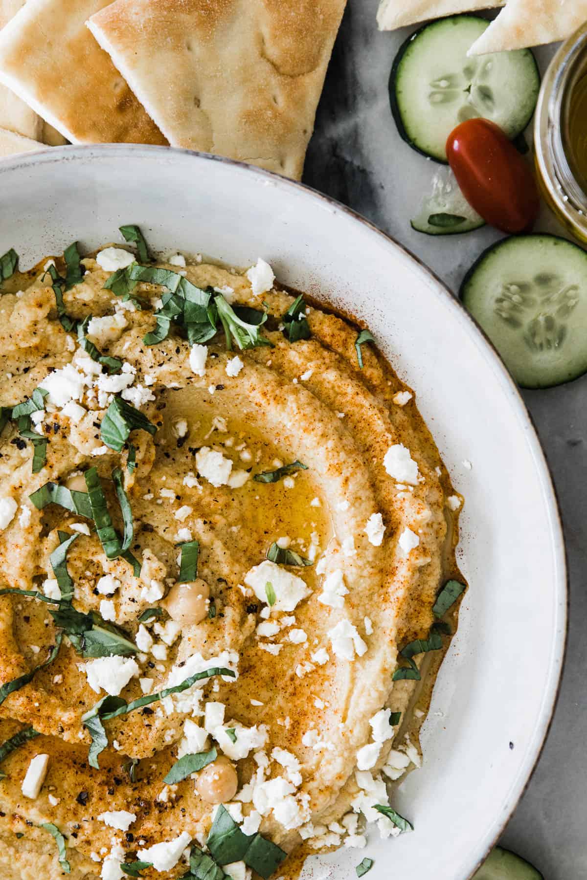 Easy hummus in a bowl topped with flakes of cheese, chopped herbs, and cracked pepper.