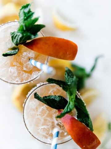 An overhead shot of peach lemonade. The glasses are rimmed with sugar and garnished with peach slices and mint.