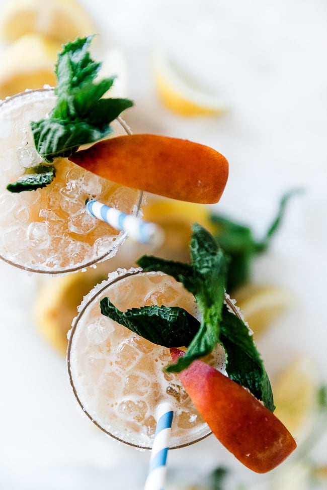 An overhead shot of peach lemonade. The glasses are rimmed with sugar and garnished with peach slices and mint.