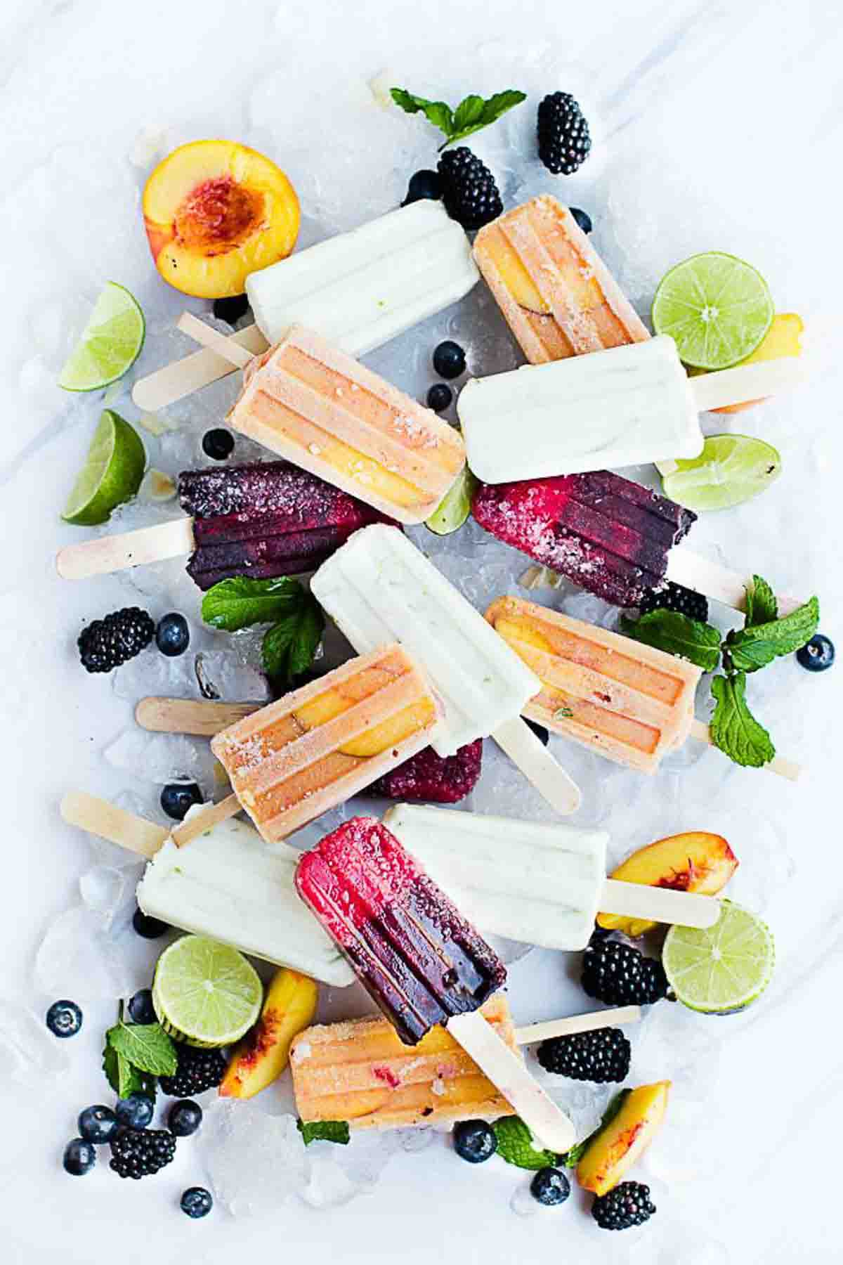 Different flavored fruit popsicles on a marble surface with ice and fresh fruit