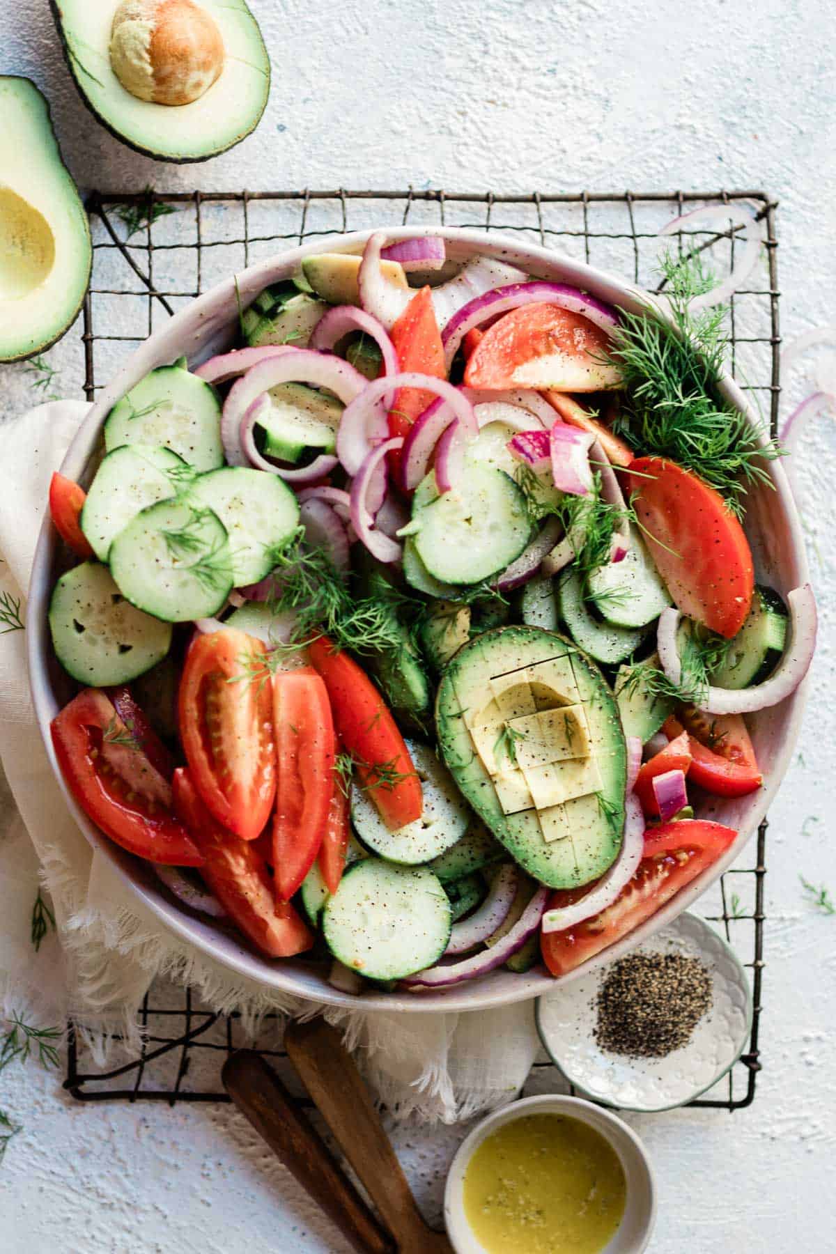Cucumber tomato red onion salad in a white salad bowl, atop a cooling rack.