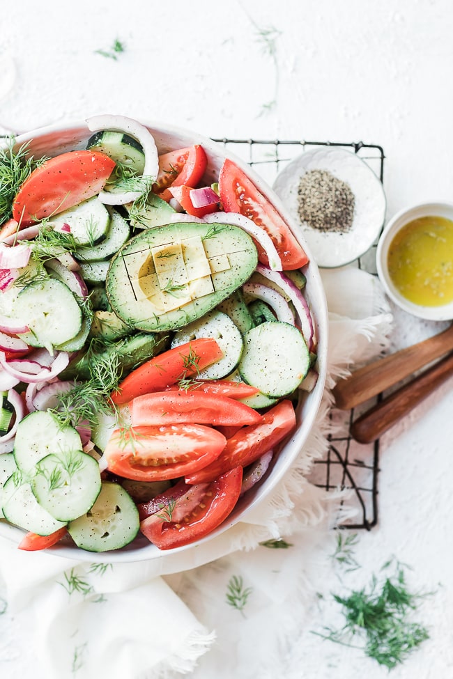 Cucumber tomato red onion salad in a white bowl, garnished with dill. Dressing on this side.