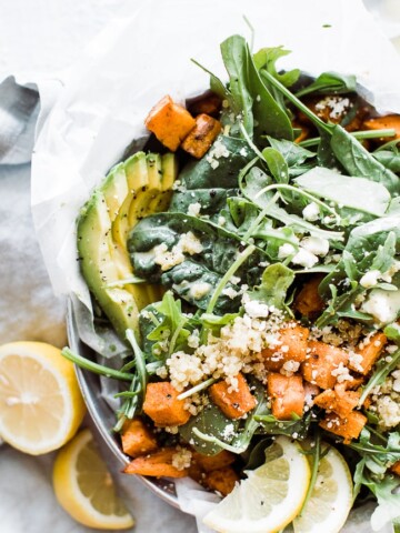 arugula salad topped with sliced avocado, dressing, roasted sweet potatoes, and cheese