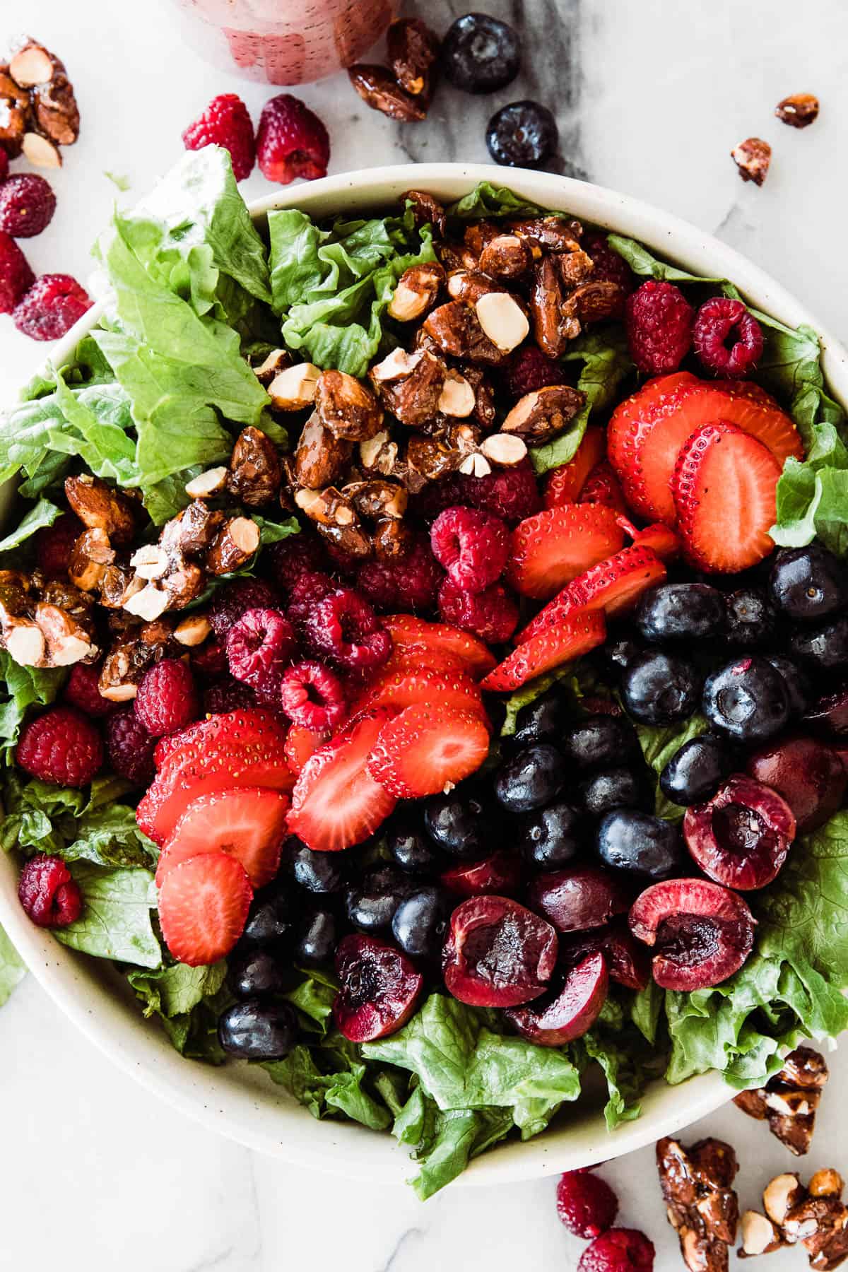 Large bowl of blue berry salad full of lettuce, almonds, and variety of berries.